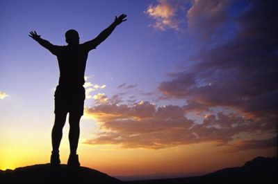 Person standing triumphantly in front of a sunset